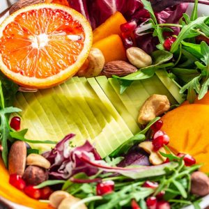 Healthy vegan lunch Buddha bowl. Avocado, avocado, persimmon, blood orange, nuts, spinach arugula and pomegranate. Food recipe background. Close up.